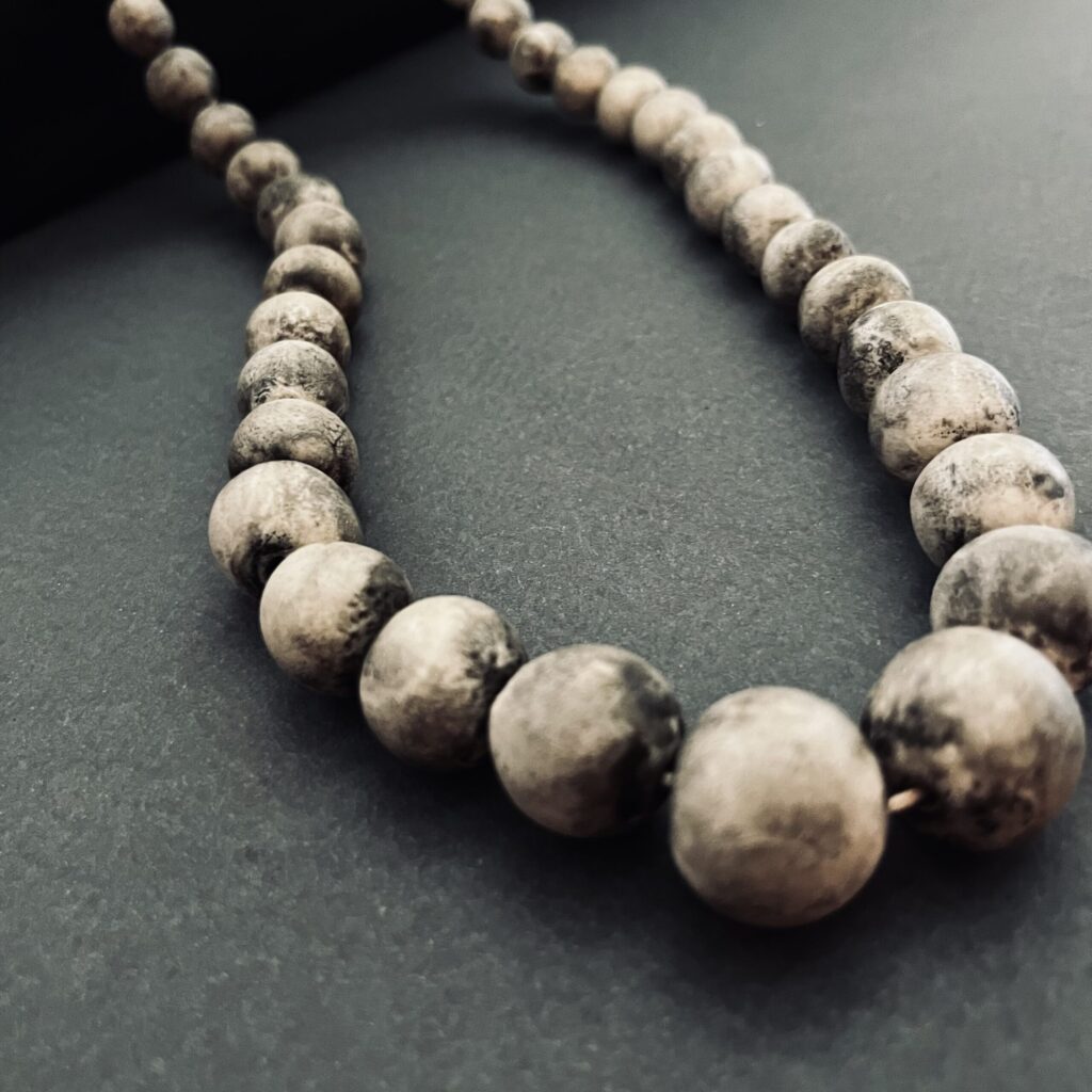 Handmade Eggshell Porcelain necklace with stone-like beads arranged on a dark background.